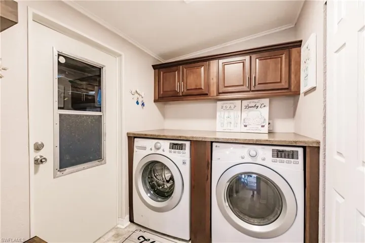 Laundry room featuring light tile patterned floors, independent washer and dryer, crown molding, and cabinets