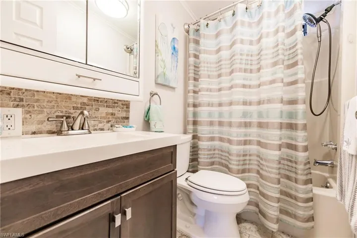 Full bathroom with backsplash, crown molding, shower / tub combo with curtain, toilet, and vanity