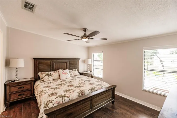 Bedroom with a textured ceiling, multiple windows, dark hardwood / wood-style flooring, and ceiling fan