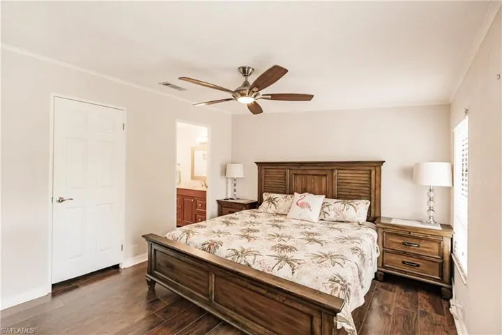 Bedroom with dark wood-type flooring, crown molding, ensuite bathroom, and ceiling fan