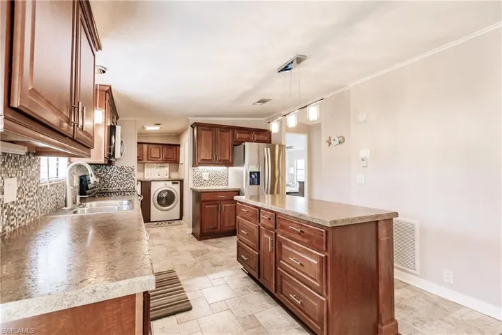 Kitchen featuring tasteful backsplash, a kitchen island, stainless steel appliances, washer / dryer, and sink