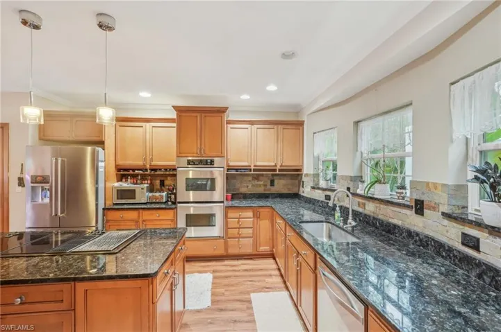 Kitchen featuring light wood-type flooring, ornamental molding, decorative backsplash, stainless steel appliances, and a sink