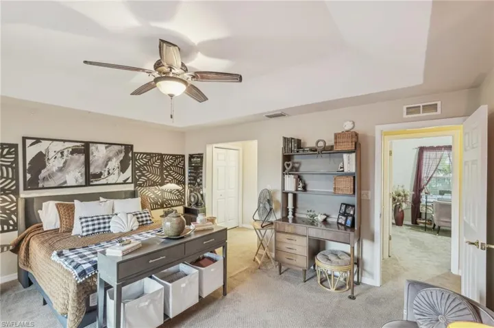 Carpeted bedroom with a raised ceiling, ceiling fan, baseboards, and visible vents