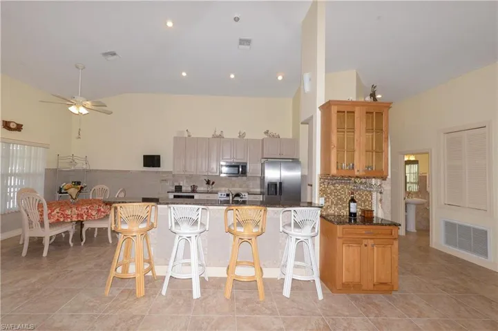 Kitchen with stainless steel appliances, a ceiling fan, dark stone counters, light tile patterned floors, and a breakfast bar
