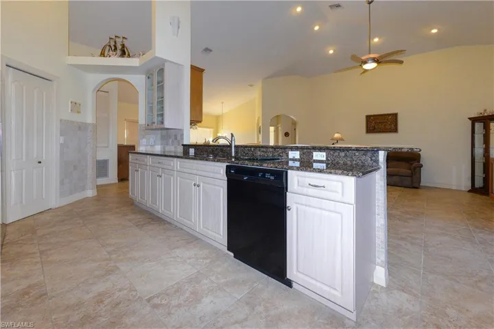 Kitchen featuring arched walkways, dark stone countertops, dishwasher, ceiling fan, and high vaulted ceiling