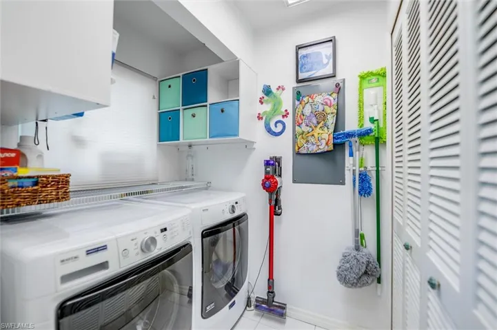 Laundry area with light tile patterned floors, washing machine and clothes dryer, and cabinet space