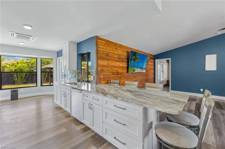 Kitchen with a kitchen bar, stainless steel dishwasher, light wood-type flooring, wooden walls, and lofted ceiling
