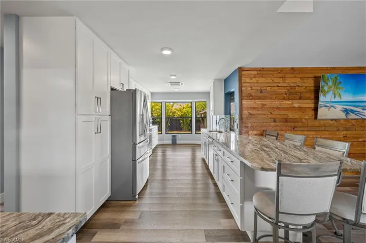 Kitchen with a breakfast bar, stainless steel refrigerator with ice dispenser, white cabinetry, and wood-type flooring