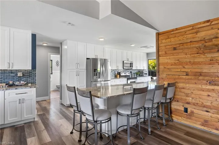 Kitchen with stone countertops, dark wood-type flooring, appliances with stainless steel finishes, and tasteful backsplash