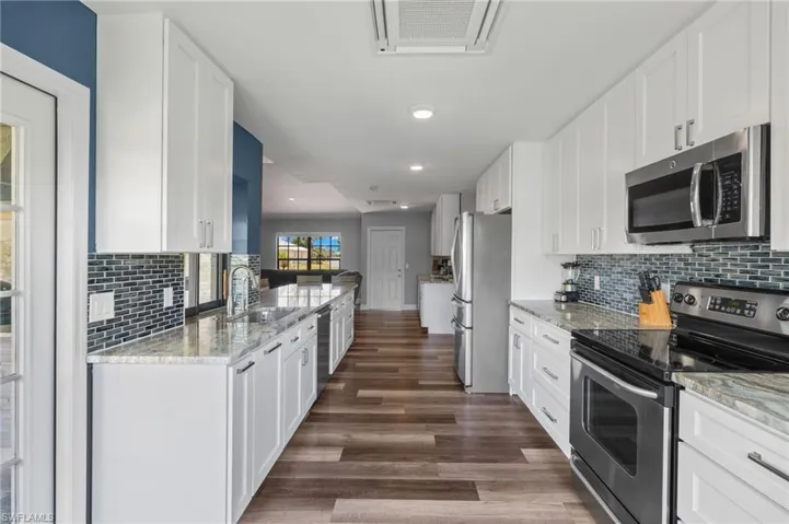 Kitchen with white cabinets, light stone counters, dark wood-type flooring, appliances with stainless steel finishes, and sink