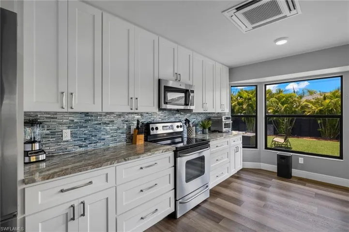 Kitchen with white cabinetry, dark stone countertops, appliances with stainless steel finishes, backsplash, and wood-type flooring