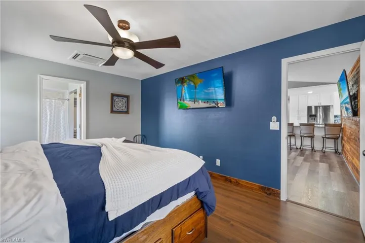 Bedroom with ceiling fan, ensuite bath, stainless steel fridge with ice dispenser, and dark hardwood / wood-style floors