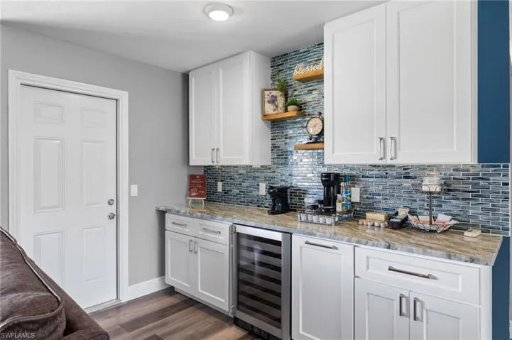 Kitchen featuring light stone counters, backsplash, wine cooler, white cabinetry, and dark wood-type flooring