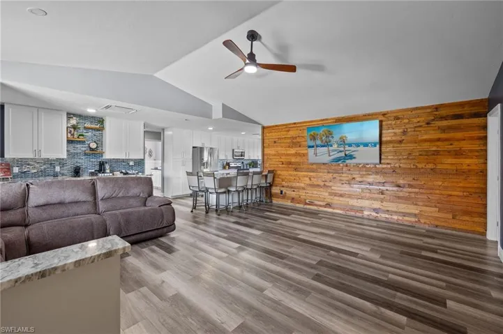 Living room with vaulted ceiling, ceiling fan, wooden walls, and hardwood / wood-style flooring