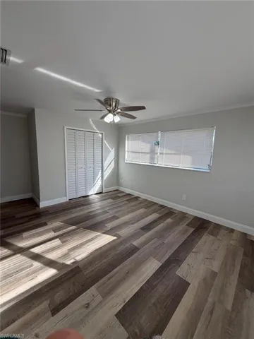 Unfurnished bedroom featuring a closet, dark wood-style floors, ornamental molding, and a ceiling fan