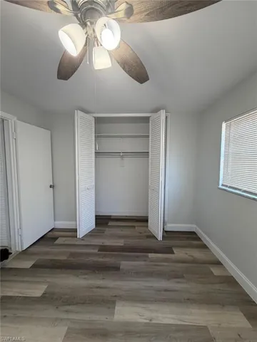Unfurnished bedroom with a closet, dark wood-style floors, and a ceiling fan