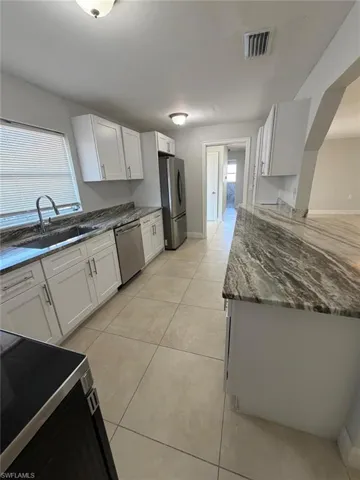 Kitchen featuring stainless steel appliances, white cabinetry, dark stone counters, and light tile patterned floors