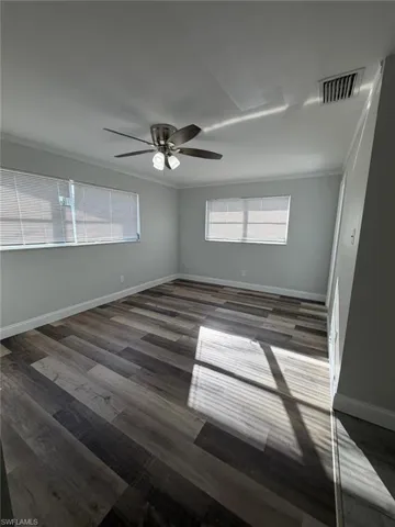 Unfurnished room with a ceiling fan, dark wood-type flooring, plenty of natural light, and ornamental molding