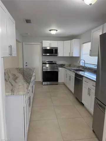 Kitchen featuring stainless steel appliances, dark stone countertops, white cabinetry, and light tile patterned floors