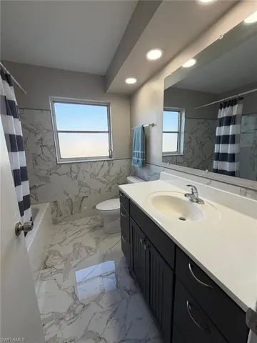 Full bath featuring tile walls, a wainscoted wall, vanity, light marble finish flooring, and recessed lighting