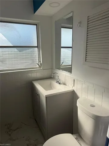 Half bathroom with vanity, tile walls, a wainscoted wall, and light marble finish floors