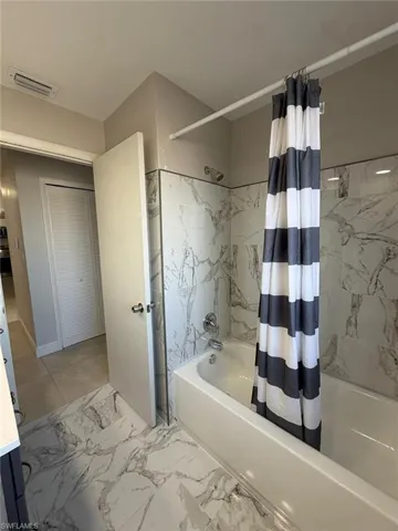 Bathroom featuring a combined bath / shower with marble appearance, vanity, and light marble finish floors