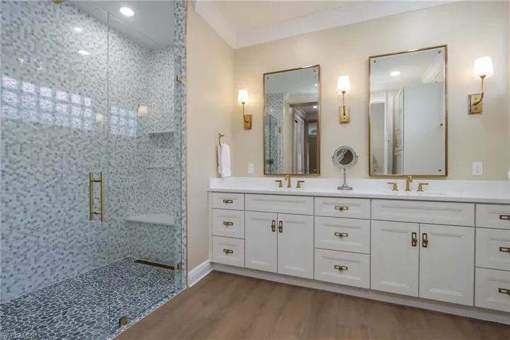 Bathroom featuring a stall shower, crown molding, double vanity, and wood finished floors