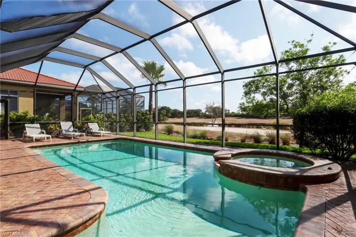 View of swimming pool featuring a patio, a pool with connected hot tub, and glass enclosure