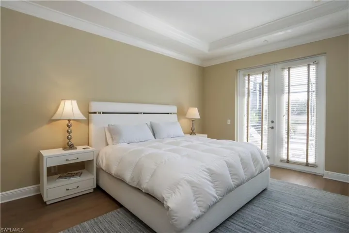 Bedroom with access to outside, wood finished floors, ornamental molding, and a tray ceiling