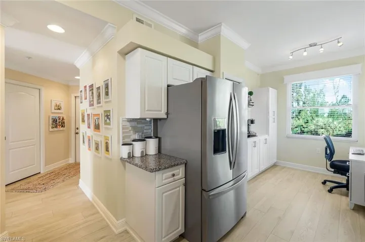 Kitchen featuring white cabinetry, crown molding, light hardwood / wood-style flooring, stainless steel fridge, and decorative backsplash