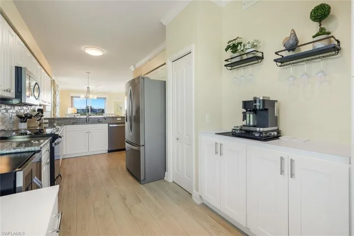 Kitchen with decorative light fixtures, white cabinets, light hardwood / wood-style floors, stainless steel appliances, and crown molding