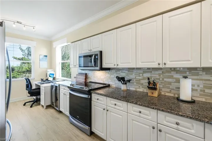 Kitchen with stainless steel appliances, white cabinetry, and dark stone countertops