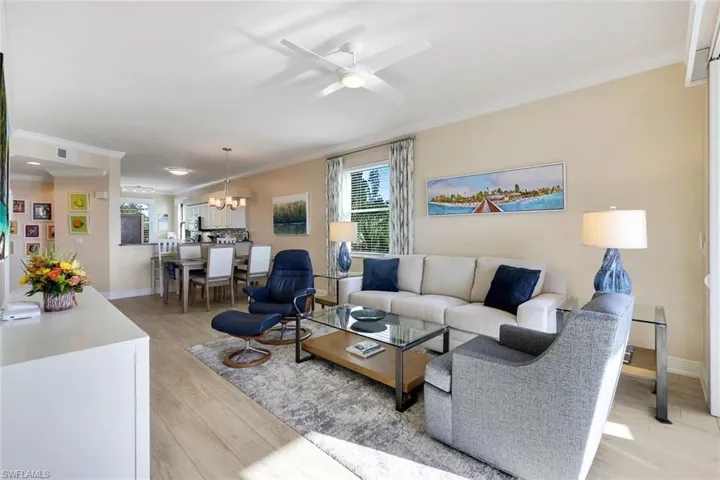 Living room with crown molding, ceiling fan with notable chandelier, and light wood-type flooring