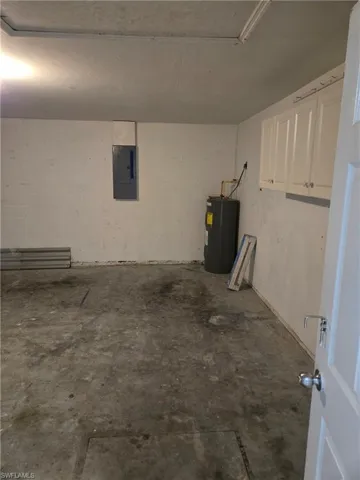 Garage featuring electric water heater, electric panel, and concrete block wall