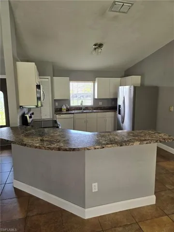 Kitchen with stainless steel fridge, white dishwasher, white cabinetry, a peninsula, and dark tile patterned floors