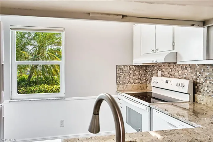 Kitchen featuring electric range, white cabinets, light stone counters, and backsplash