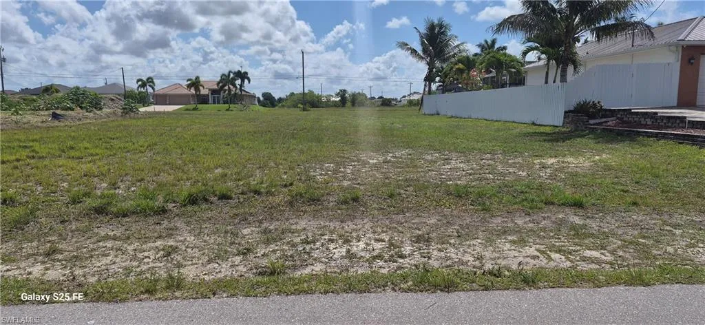 Expansive undeveloped lot featuring a grass and sand surface, bordered by a paved road