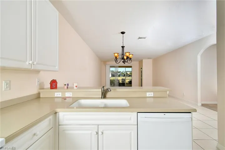 Kitchen featuring a peninsula, dishwasher, arched walkways, white cabinetry, and suspended lighting