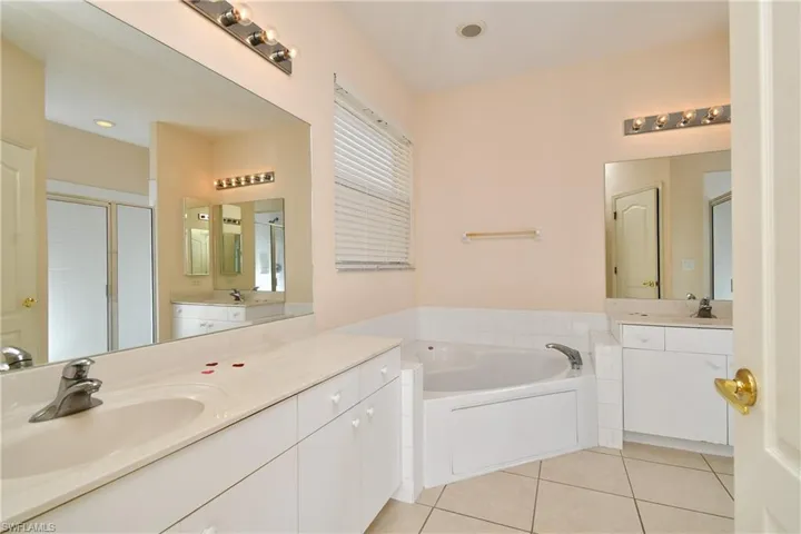Bathroom featuring a garden tub, a shower stall, two vanities, and light tile patterned floors