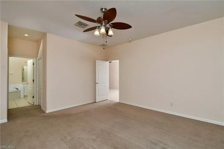 Unfurnished bedroom featuring light colored carpet, connected bathroom, and ceiling fan