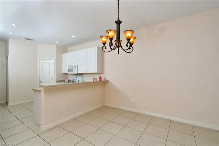 Kitchen featuring a peninsula, white cabinetry, hanging lights, light countertops, and white appliances