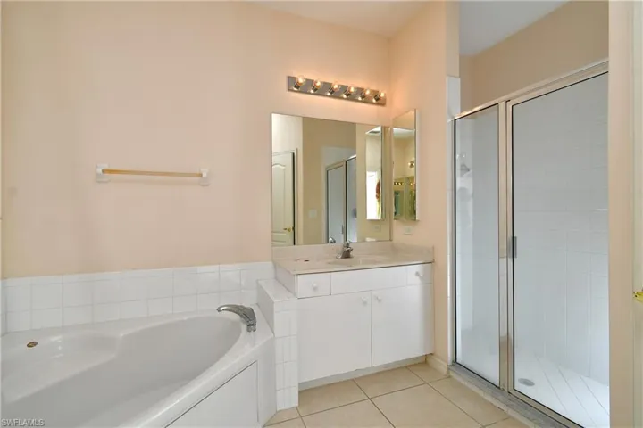Full bath featuring a shower stall, a garden tub, light tile patterned floors, and vanity