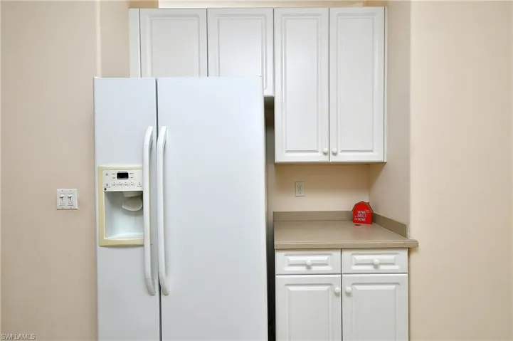 Kitchen featuring white refrigerator with ice dispenser, white cabinets, and light countertops