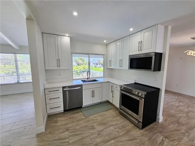Kitchen featuring appliances with stainless steel finishes, white cabinets, light stone counters, beam ceiling, and recessed lighting