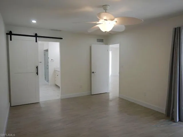 Unfurnished bedroom with a barn door, ensuite bathroom, a ceiling fan, light wood-style floors, and recessed lighting