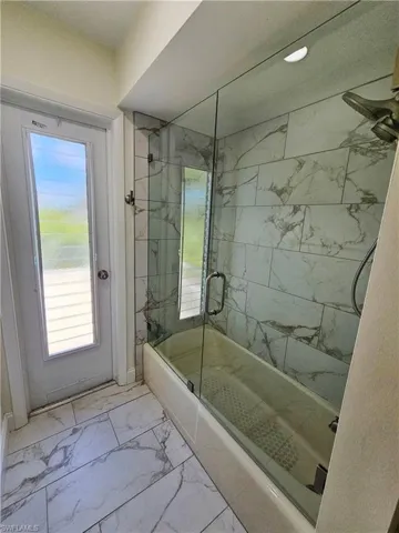 Bathroom with light marble finish floors and enclosed tub / shower combo