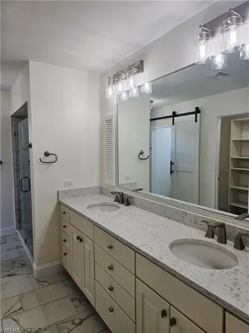 Bathroom with double vanity, light marble finish flooring, a shower stall, and a walk in closet
