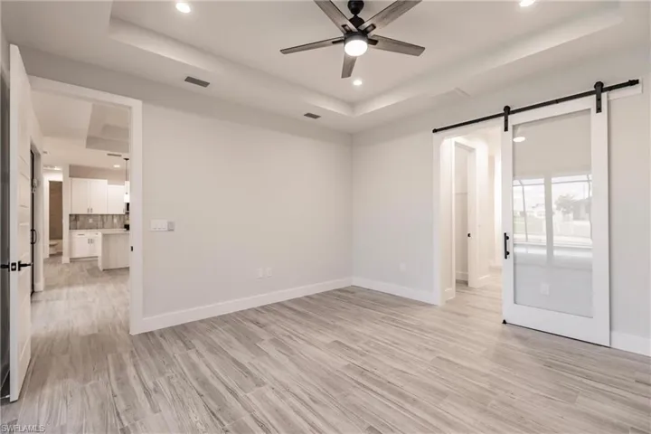Unfurnished room featuring ceiling fan, a tray ceiling, a barn door, and light hardwood / wood-style floors