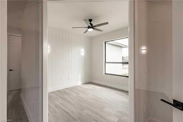 Spare room with light wood-type flooring, wooden walls, and ceiling fan