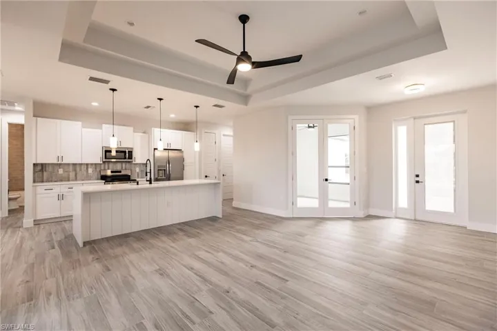 Kitchen featuring white cabinets, appliances with stainless steel finishes, a tray ceiling, and an island with sink